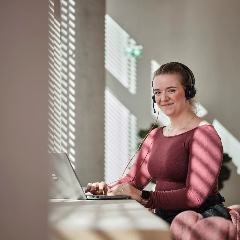JobRad-Mitarbeiterin mit rotem shirt sitzt am Laptop und lächelt dich an JobRad-Mitarbeiterin mit rotem shirt sitzt am Laptop und lächelt dich an