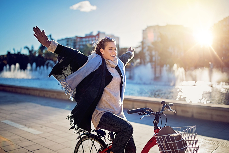 Junge Frau radelt freihändig, mit offenen Armen im Sonnenuntergang. Es ist Winter und es liegt Schnee. Junge Frau radelt freihändig, mit offenen Armen im Sonnenuntergang. Es ist Winter und es liegt Schnee.